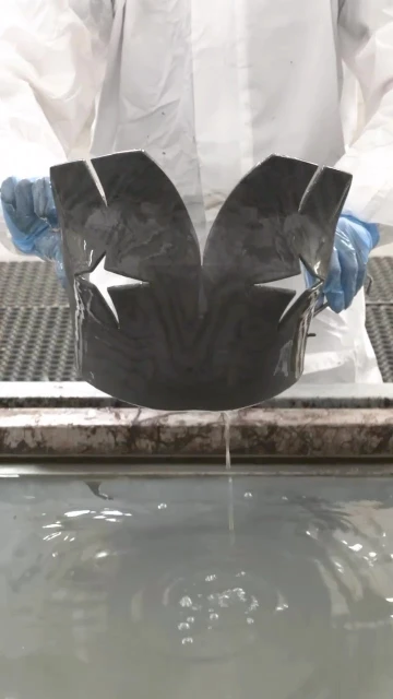 Craftsperson holding wet industrial component with white stars cut out in an indoor environment, with visible water and white clothing.