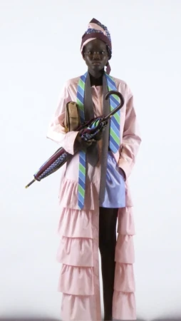 Model in pink layered coat holding an umbrella and handbag against a plain white background by photographer Michele Foti