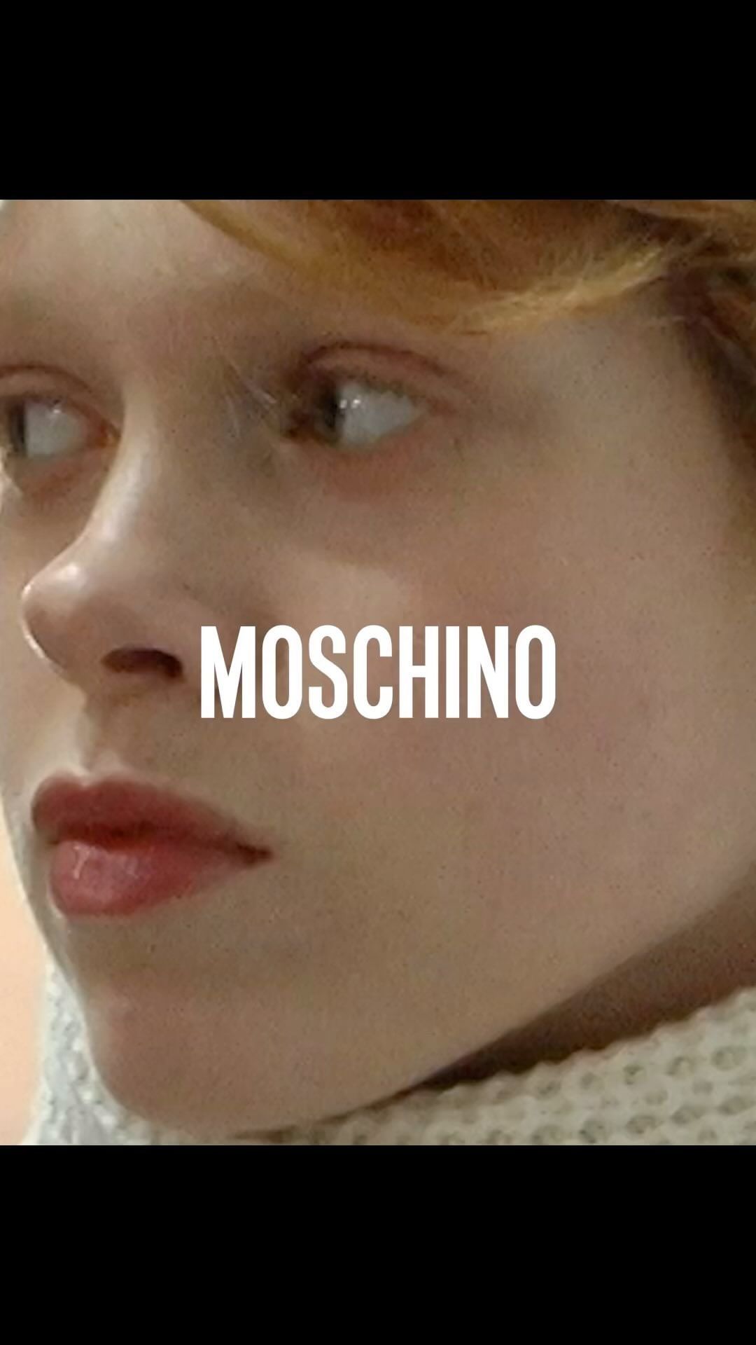 Close-up shot of a young fair-skinned person with freckles, neutral expression, and white Moschino text overlay against a blurred background.
