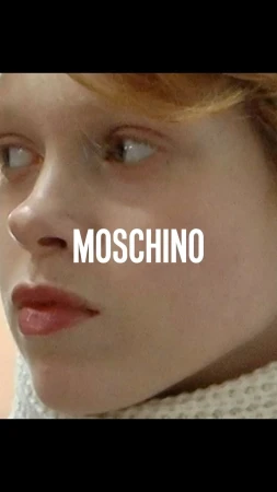 Close-up shot of a young fair-skinned person with freckles, neutral expression, and white Moschino text overlay against a blurred background.