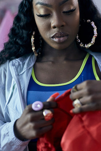 Close-up of stylish African-American woman with long curly hair, hoop earrings, vibrant blue and green top, and a light jacket indoors.