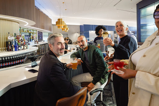Group of diverse adults socializing and toasting with drinks at an upscale bar with modern decor, featuring varied beverages and lighting.