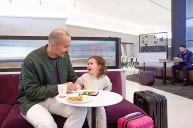 Man and young child seated on purple sofa in hotel lobby with luggage