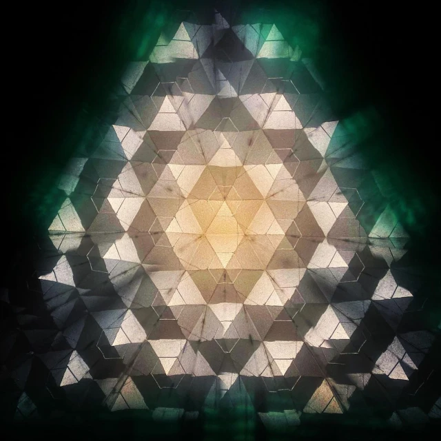 Abstract geometric pattern with triangle shapes and a central glow, creating a kaleidoscope-like effect in shades of green, beige, and black.