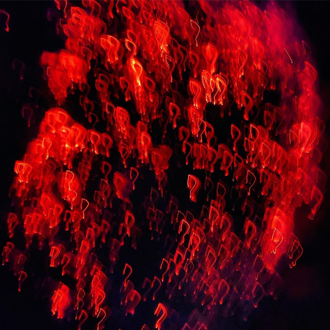 Abstract image of blurred, glowing red question marks on a black background, creating a sense of mystery and intrigue.
