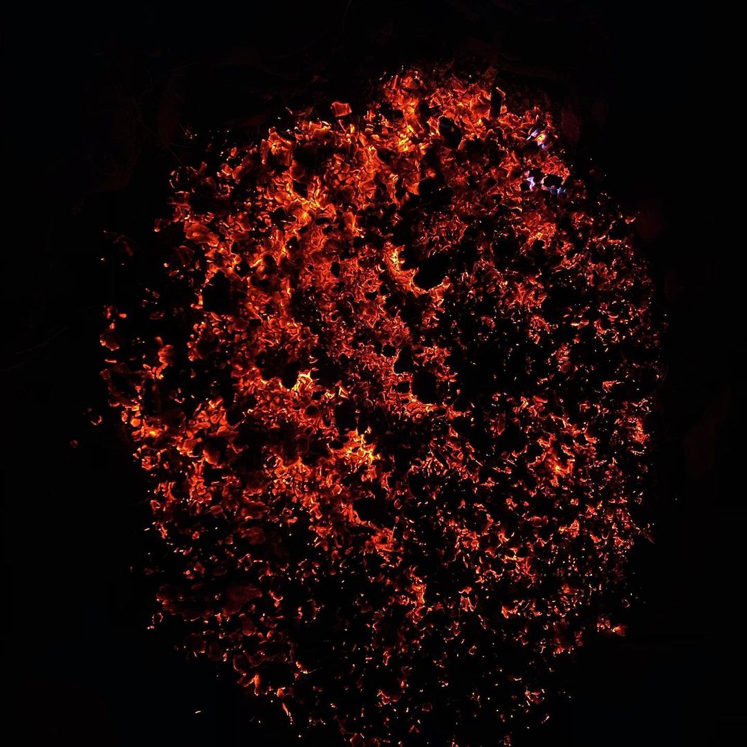A cluster of fiery embers and sparks glows intensely against a black background, resembling a burning galaxy or abstract fire pattern.