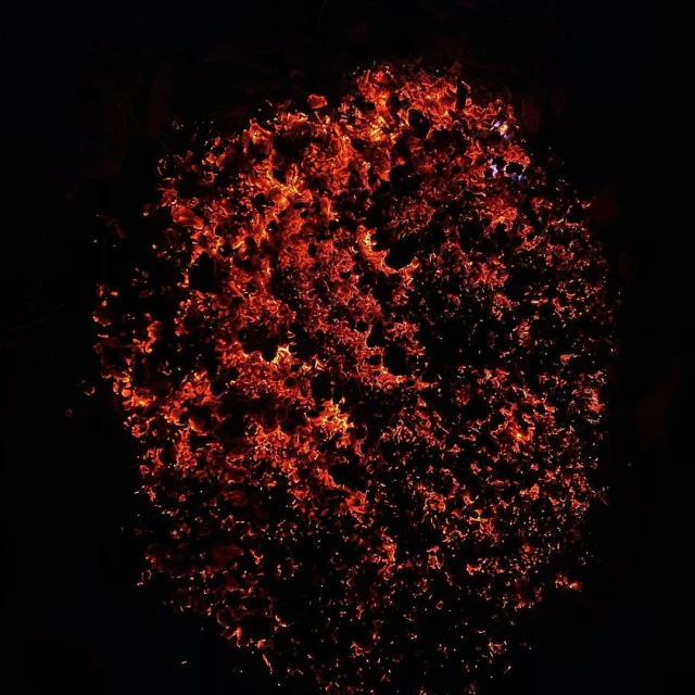 A cluster of fiery embers and sparks glows intensely against a black background, resembling a burning galaxy or abstract fire pattern.
