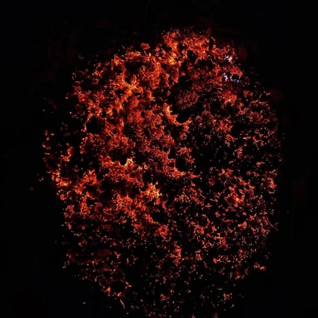 A cluster of fiery embers and sparks glows intensely against a black background, resembling a burning galaxy or abstract fire pattern.