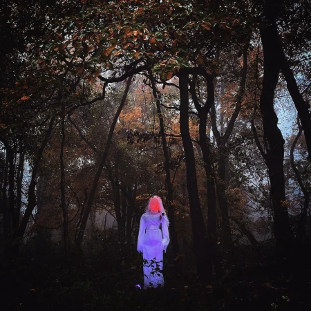 Person in white outfit with glowing head standing in a foggy forest at night, creating an eerie and mysterious Halloween scene.