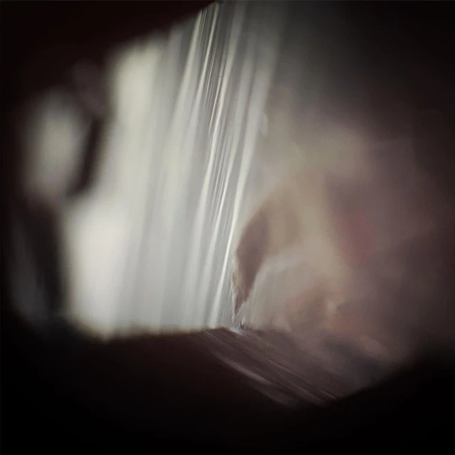 Abstract macro photograph showing blurred light refracting through a transparent plastic material with dark surroundings, close up view.