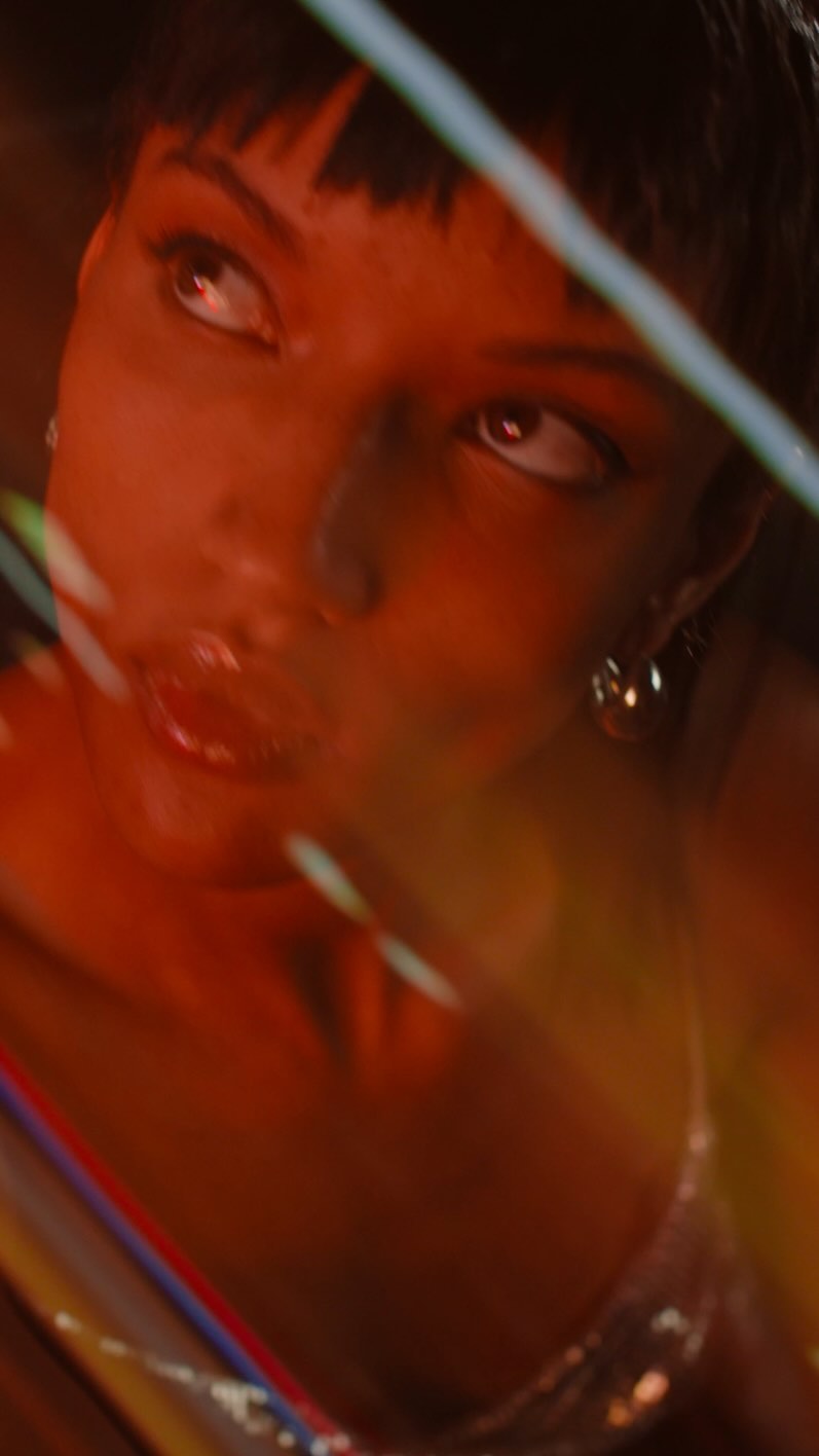 Close-up of a brunette woman in an orange-lit indoor setting, featuring soft light and a shallow depth of field, with a hint of reflective material.