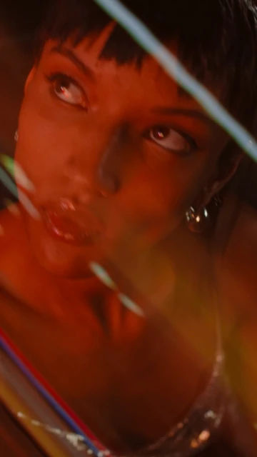 Close-up of a brunette woman in an orange-lit indoor setting, featuring soft light and a shallow depth of field, with a hint of reflective material.