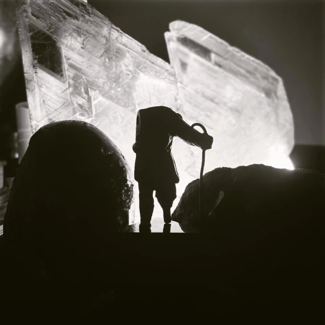 Silhouette of a person with a cane standing between two dark rocks, with a large crystal formation in the background.