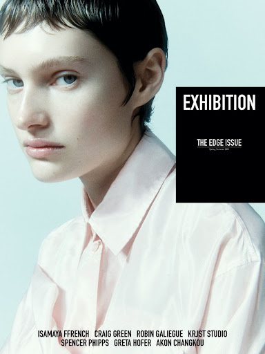 Exhibition Magazine cover featuring a model with a short dark haircut wearing a pink collared shirt on a light blue background.