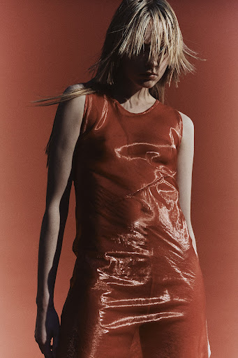 Fashion shot of a blonde adult woman wearing a shiny red dress, posing in front of a red background. Studio lighting is visible.