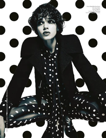 Editorial fashion shot of a young adult in a black coat and polka dot shirt and tights against a black and white polka dot background.