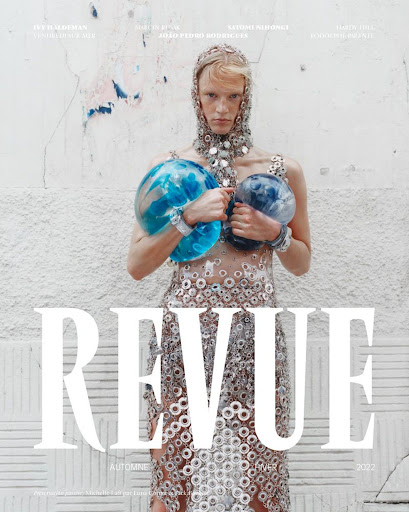Fashion magazine cover featuring a person holding translucent blue spheres, adorned with metallic accents, set against a textured wall.
