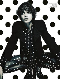 Model with short dark hair in a black structured jacket and polka dot blouse against a large polka dot backdrop