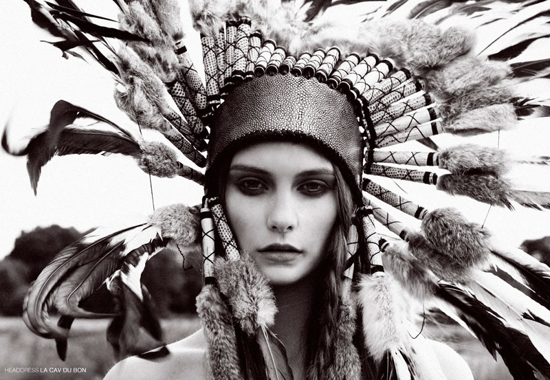Monochrome portrait of a woman wearing an elaborate feathered headdress, captured in a photo studio setting with soft, diffused lighting.