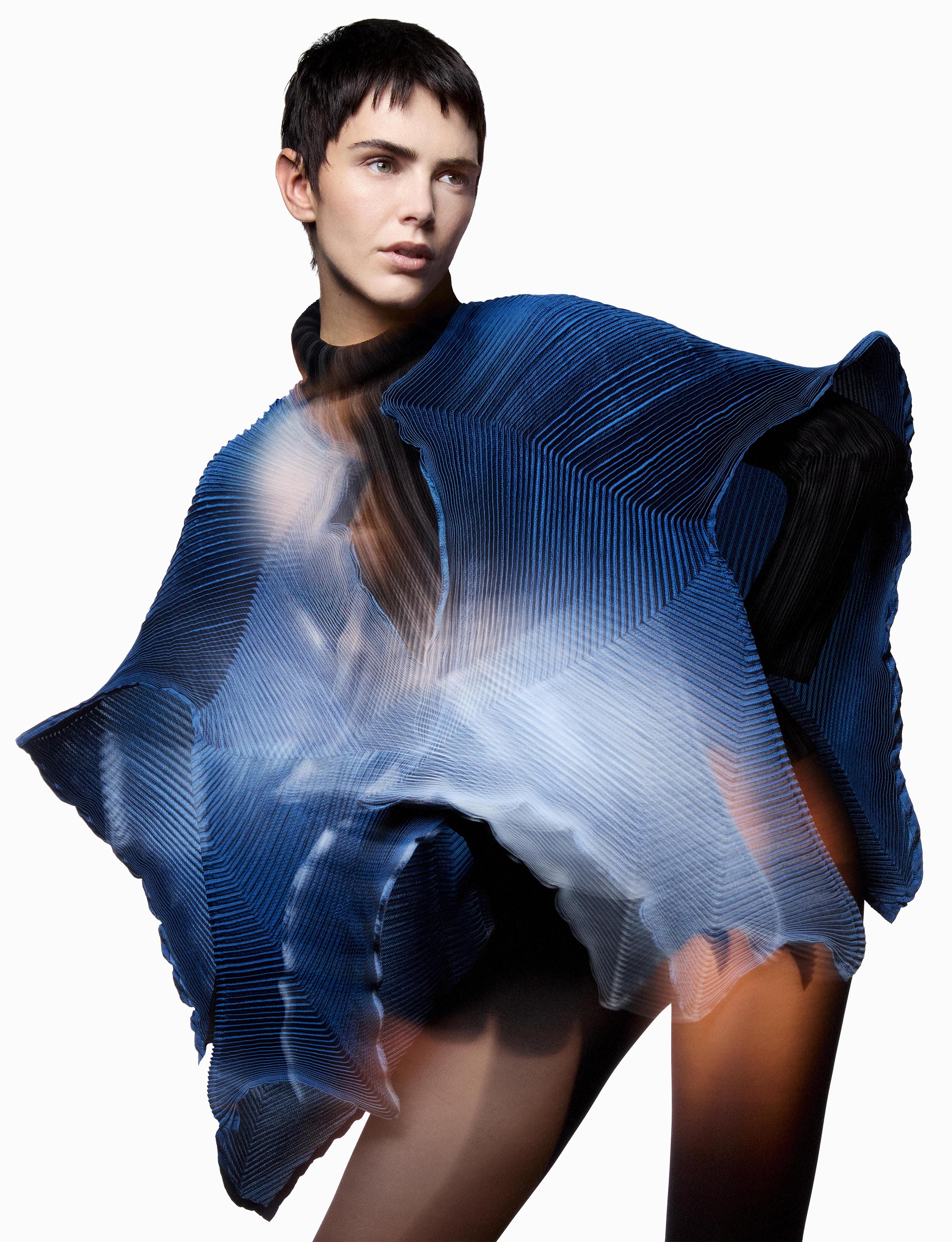 Fashion shot of a model wearing a blue and white textured, layered top in a studio setting with bright, neutral lighting.