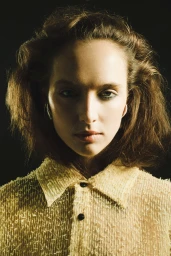 Portrait of a woman with textured brown hair wearing a textured light-colored collared shirt against a dark background