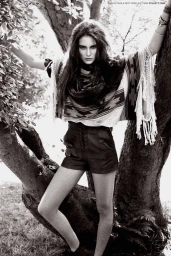 Model with long dark hair wearing a patterned fringe poncho and high waisted shorts posed between large tree trunks