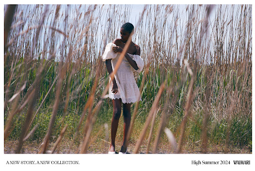 Fashion shot of a young African American woman in a white eyelet dress standing in a field of tall grasses on a sunny day.