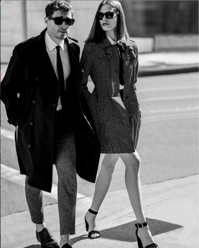 Black and white portrait of a man in a dark trench coat and a woman in a patterned coat walking outdoors