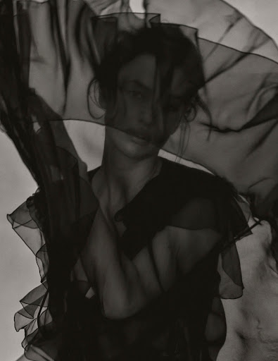 Monochrome portrait of a woman with a sheer dark fabric draped partially over her face in a studio, creating a soft, artistic effect.
