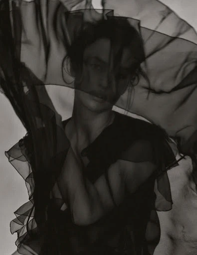 Monochrome portrait of a woman with a sheer dark fabric draped partially over her face in a studio, creating a soft, artistic effect.