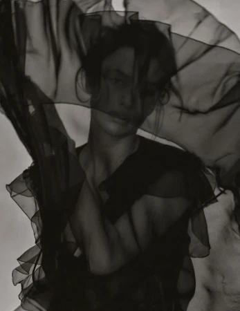 Monochrome portrait of a woman with a sheer dark fabric draped partially over her face in a studio, creating a soft, artistic effect.