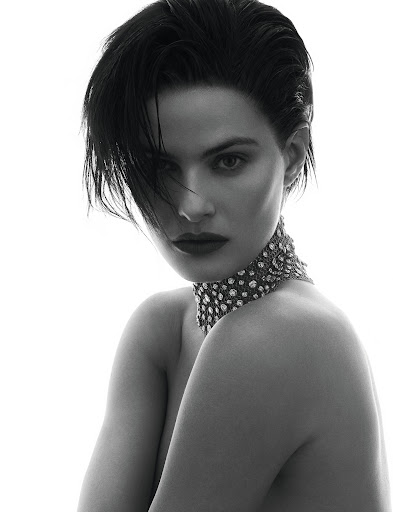 Monochrome studio portrait of a young adult woman with short dark hair wearing a jeweled choker against a white backdrop.