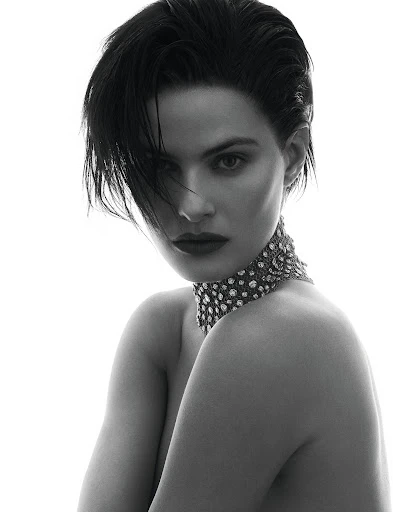 Monochrome studio portrait of a young adult woman with short dark hair wearing a jeweled choker against a white backdrop.
