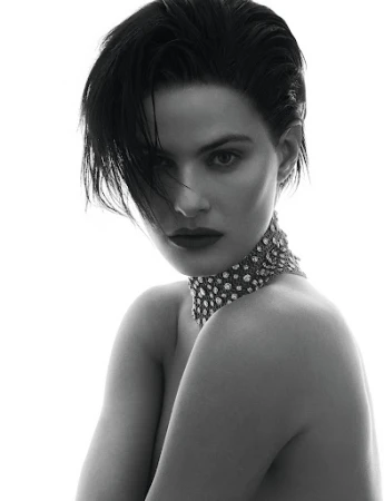 Monochrome studio portrait of a young adult woman with short dark hair wearing a jeweled choker against a white backdrop.