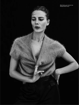 Monochrome portrait of a woman in a fuzzy short sleeve V-neck top and dark trousers against a black background