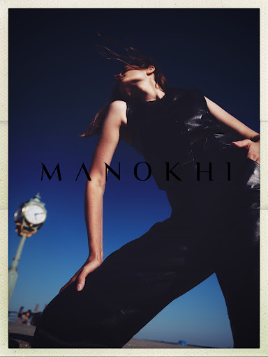 Fashion shot of a woman in black clothing posing outdoors with a clock tower in the background and a dark blue sky overhead.