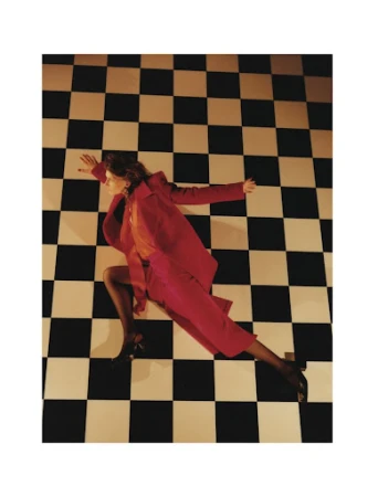 Fashion photograph featuring a woman in a red suit lying on a checkered floor, with her arms outstretched and legs bent.
