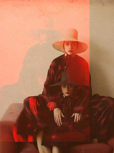 Two women in vintage-style dresses and hats pose indoors with a blurred, layered effect, creating a retro and artistic fashion image.
