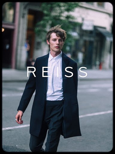 A young man in a dark overcoat and white shirt walking on a city street