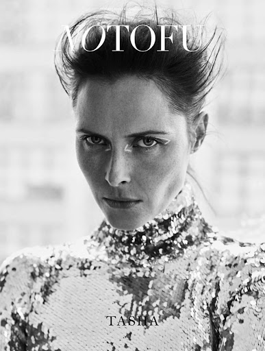 Monochrome portrait of a woman with slicked-back hair, wearing a sparkly top, looking at the camera, and the text "AYOTOFU" above her head.