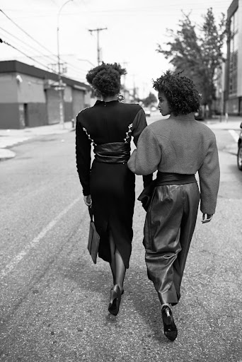 Two adult women walking down a city street in fashionable clothing, captured in a black and white photograph with urban background.