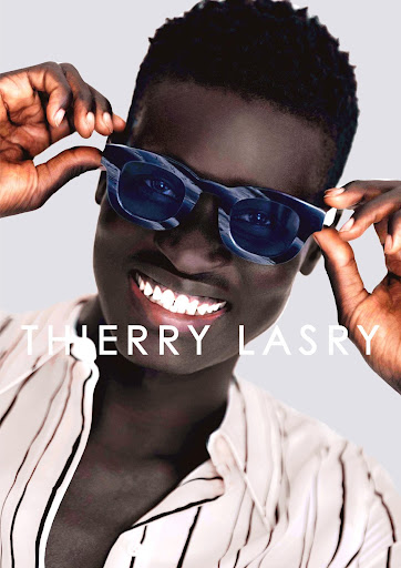 Headshot of an African male model smiling and wearing blue-and-white patterned sunglasses and a vertically striped button-down shirt.