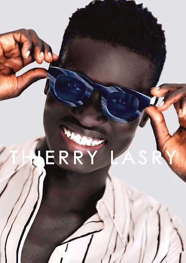 Headshot of an African male model smiling and wearing blue-and-white patterned sunglasses and a vertically striped button-down shirt.