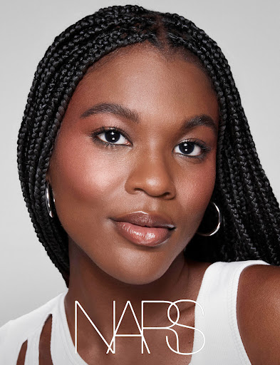 Portrait of a woman with braided hair wearing makeup and jewelry. The NARS logo is visible in the lower portion of the image.