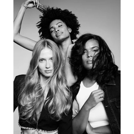 Black and white portrait of three diverse female models posing closely together against a seamless grey backdrop