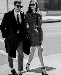 Black and white portrait of a man in a dark trench coat and a woman in a patterned coat walking outdoors