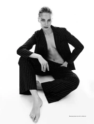 Model seated on white background wearing a black pinstripe suit jacket and matching trousers styled by Anna Katsanis.