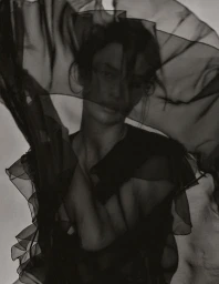 Model draped in sheer black fabric holding a dark veil over her face, styled by Anna Katsanis.