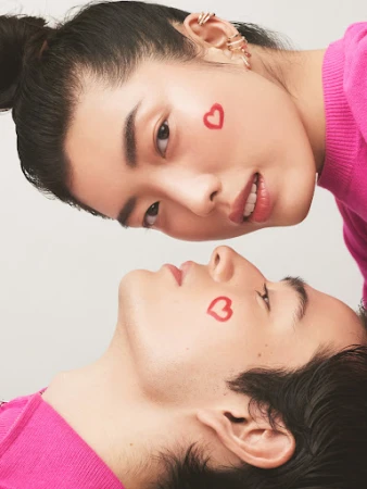 Close-up portrait of two young models with heart drawings on their cheeks wearing pink sweaters against a white background