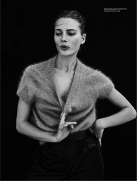 Monochrome portrait of a woman in a fuzzy short sleeve V-neck top and dark trousers against a black background